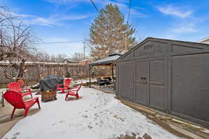 Snow covered patio featuring a gazebo, a storage shed, a fire pit, and grilling area