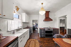 Kitchen with wall chimney exhaust hood, white cabinetry, butcher block counters, stainless steel appliances, and sink