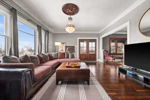 Living room featuring french doors, dark hardwood / wood-style floors, crown molding, and a notable chandelier