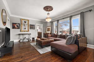 Living room featuring dark wood-type flooring, ornamental molding, and a notable chandelier