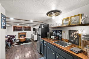 Kitchen with a textured ceiling, dark hardwood / wood-style flooring, blue cabinetry, sink, and butcher block countertops