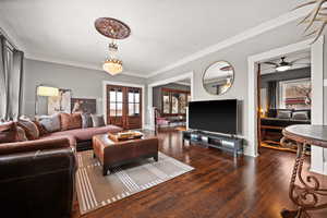 Living room with ceiling fan with notable chandelier, dark hardwood / wood-style flooring, ornamental molding, and french doors