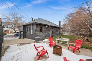 Snow covered house with an outdoor fire pit, central air condition unit, and a patio