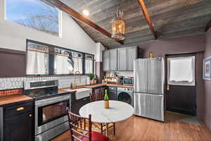 Kitchen with washer / dryer, stainless steel appliances, sink, pendant lighting, and beamed ceiling