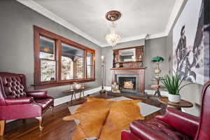 Living room with a premium fireplace, crown molding, hardwood / wood-style flooring, and an inviting chandelier