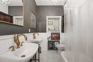 Bathroom featuring tile patterned floors, a bathtub, double sink, toilet, and a notable chandelier