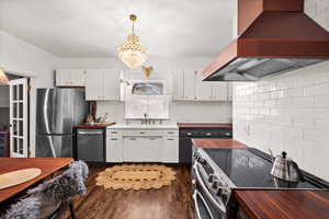 Kitchen featuring white cabinets, decorative light fixtures, stainless steel appliances, tasteful backsplash, and island range hood