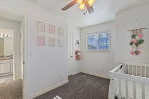 Carpeted bedroom featuring ensuite bathroom, a textured ceiling, sink, a nursery area, and ceiling fan