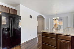 Kitchen featuring pendant lighting, an inviting chandelier, dark hardwood / wood-style floors, fridge with ice dispenser, and dark brown cabinets