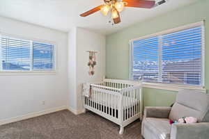 Bedroom with ceiling fan, a nursery area, and carpet flooring