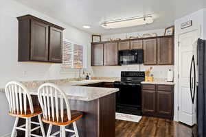 Kitchen with black appliances, sink, kitchen peninsula, a breakfast bar area, and dark hardwood / wood-style floors