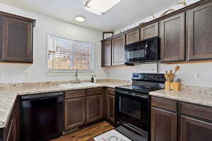 Kitchen featuring black appliances, light stone countertops, dark brown cabinets, sink, and dark wood-type flooring