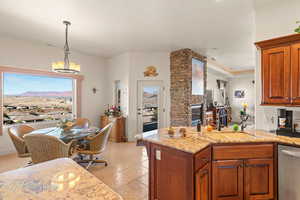 Kitchen featuring dishwasher, hanging light fixtures, sink, a stone fireplace, and light stone counters