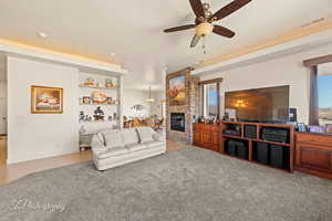 Living room featuring ceiling fan, a textured ceiling, light tile patterned floors, and a stone fireplace