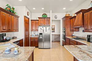 Kitchen featuring custom range hood, light tile patterned floors, light stone countertops, and stainless steel appliances