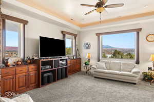 Carpeted living room featuring ceiling fan, plenty of natural light, and a raised ceiling