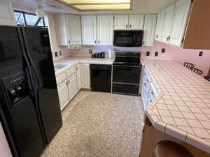 Kitchen featuring black appliances, white cabinetry, light tile patterned floors, and tile counters