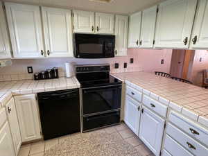 Kitchen with black appliances, white cabinetry, and tile countertops