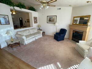 Living room with light carpet, ceiling fan, a textured ceiling, and lofted ceiling