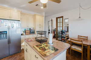 Kitchen featuring a center island, cream cabinetry, pendant lighting, ceiling fan, and stainless steel fridge