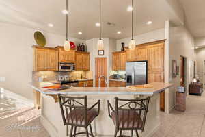 Kitchen featuring a kitchen bar, appliances with stainless steel finishes, a spacious island, hanging light fixtures, and decorative backsplash