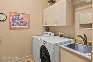 Clothes washing area with cabinets, washer and clothes dryer, and sink