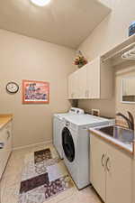 Laundry room featuring light tile patterned floors, cabinets, washer and clothes dryer, and sink