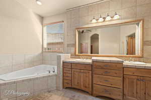 Bathroom featuring vanity, tile walls, tiled bath, and tile patterned flooring