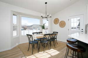 Dining area with light wood-type flooring, vaulted ceiling, and a notable chandelier