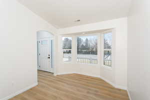 Empty room with light hardwood / wood-style flooring, lofted ceiling, and a healthy amount of sunlight