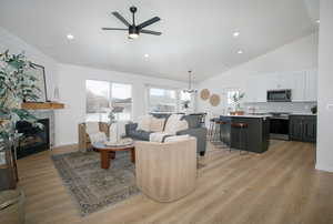 Living room with ceiling fan with notable chandelier, vaulted ceiling, and light wood-type flooring