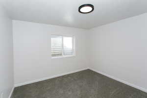 Unfurnished room with a textured ceiling and dark carpet