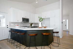 Kitchen with sink, backsplash, white cabinetry, a breakfast bar, and high vaulted ceiling