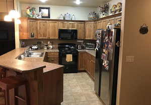 Kitchen with black appliances, decorative light fixtures, sink, kitchen peninsula, and a breakfast bar area