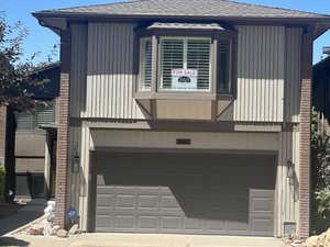 Rear view of house featuring roof with shingles, a garage, and concrete driveway