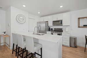 Kitchen featuring appliances with stainless steel finishes, sink, light wood-type flooring, white cabinetry, and a breakfast bar area