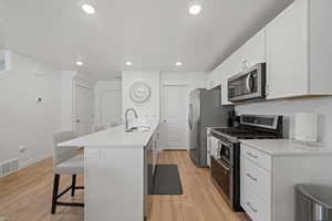 Kitchen with light hardwood / wood-style floors, appliances with stainless steel finishes, white cabinetry, sink, and a breakfast bar