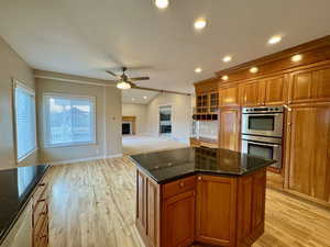 Kitchen featuring ceiling fan, light wood-type flooring, a center island, dark stone countertops, and stainless steel double oven