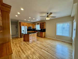 Kitchen featuring ceiling fan, light wood-type flooring, a kitchen island, decorative backsplash, and stainless steel appliances