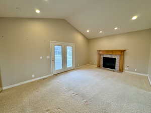 Unfurnished living room with light colored carpet, a fireplace, and lofted ceiling