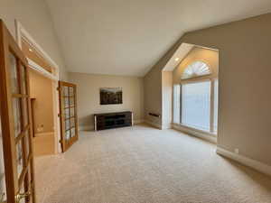 Unfurnished living room featuring light colored carpet, lofted ceiling, and a healthy amount of sunlight