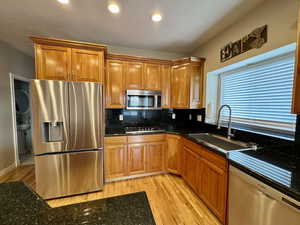 Kitchen with light hardwood / wood-style floors, sink, dark stone countertops, backsplash, and stainless steel appliances