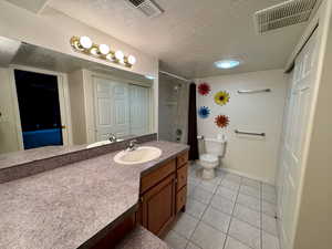 Bathroom with a textured ceiling, tile patterned floors, vanity, toilet, and a tile shower