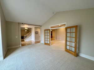 Unfurnished living room featuring light carpet, an inviting chandelier, vaulted ceiling, and french doors