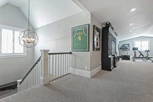 Hall with a notable chandelier, vaulted ceiling, and carpet