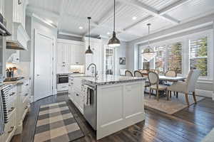 Kitchen featuring pendant lighting, white cabinets, tasteful backsplash, a kitchen island with sink, and light stone counters