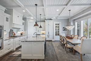 Kitchen featuring pendant lighting, dark wood-type flooring, light stone countertops, a center island with sink, and stainless steel gas cooktop