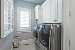 Laundry area with washing machine and dryer, cabinets, and light tile patterned flooring