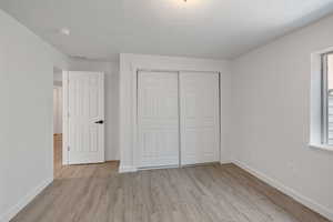 Unfurnished bedroom with light hardwood / wood-style floors, a textured ceiling, and a closet