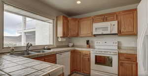 Kitchen featuring sink, light tile patterned floors, white appliances, tile countertops, and a textured ceiling